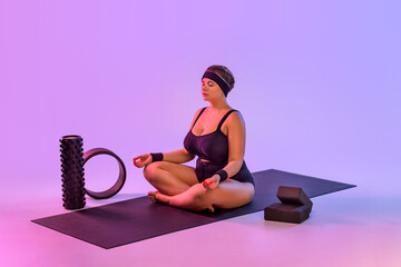 Portrait of fat young woman practicing yoga indoor. Beautiful size plus model practice asana in...