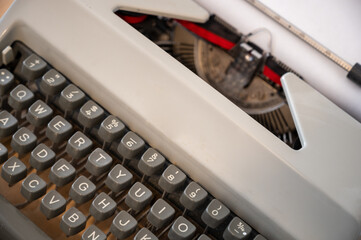 A Close Up Of A Mechanical Typewriter. The ribbon is tightly pressed against the white paper, waiting for the typist to choose which alphanumeric character is going to be imprinted on it next. - obrazy, fototapety, plakaty