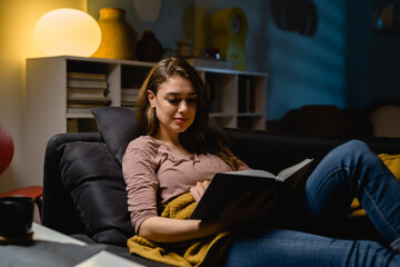 woman reading book while sitting on sofa at home