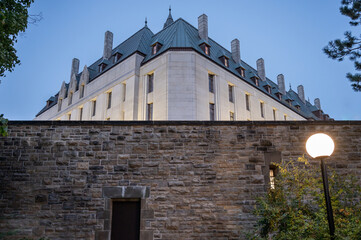 A Large Building Presides Over A Stone Wall Lit Up By A Single Lamp. This is the Supreme Court of Canada, located in Ottawa, Ontario, Canada.