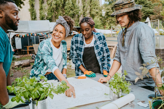 Smiling female environmentalist discussing with volunteers over blueprint at garden - Powered by Adobe