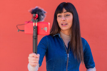 Brunette girl recording a vlog in a blue denim outfit. Caucasian pretty a red background