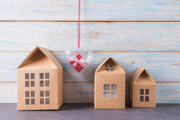 Red gift box in heart shaped container and toy houses over light wooden background
