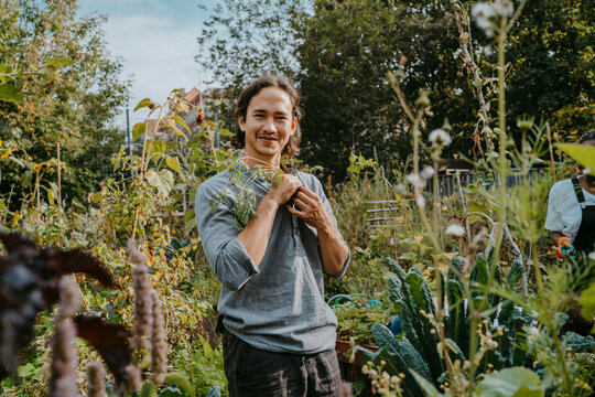 Portrait of smiling male agricultural shareholder with plant in urban garden