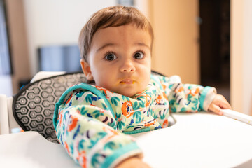Feeding his seven-month-old baby at home, his first vegetable purees, first-person view of the father spooning pumpkin, carrot and potato puree into his mouth
