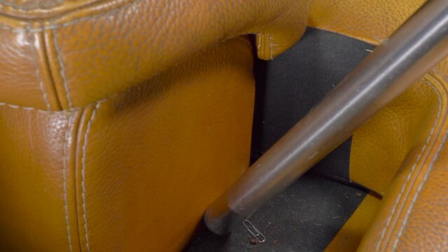 Closeup Overhead Shot Of A Man’s Hand Pulling A Brown / Tan Leather Sofa Cushion Forward, Then Using A Vacuum Cleaner Hose / Tube To Suck Up Assorted Mess Which Has Fallen Between The Gap.