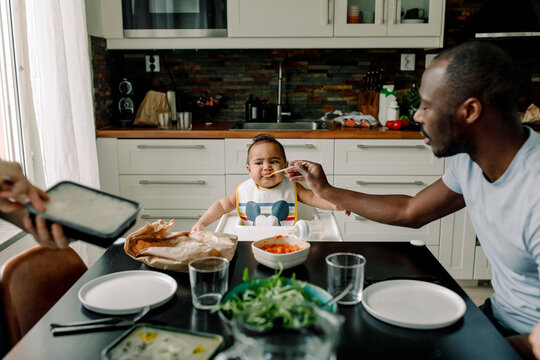 Father feeding baby boy at dining table in kitchen
