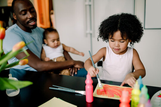 Girl painting with watercolor by father and brother at home - Powered by Adobe