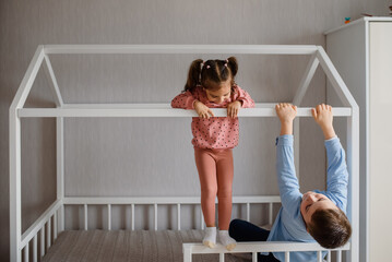 Two Children brother and sister are sitting in a Montessori bed and looking at each other and playing.