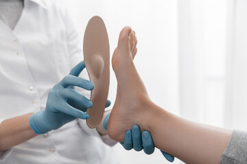 Orthopedic insole on a white background. Hands in rubber gloves hold an orthopedic insole. Foot...