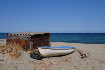 Rusty beach hut and old fishing boat on the beach in Corsica, France.