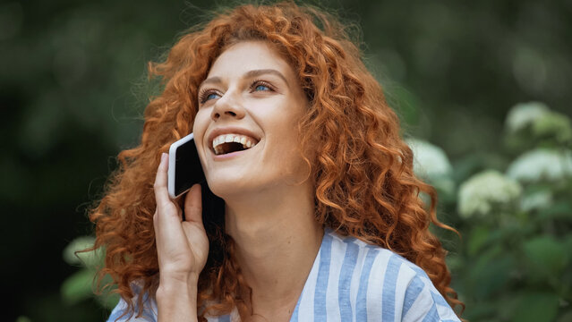 happy young woman with red hair laughing while talking on smartphone.