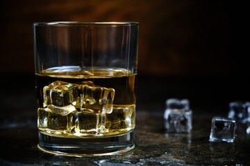 Glass chilled whiskey with ice cubes on wooden background in cellar.