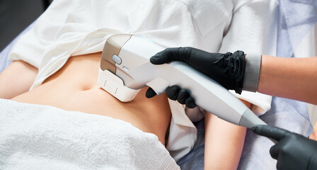 Close up doctor cosmetologist using ultrasound device while performing lifting procedure on woman abdomen. Female patient receiving body tightening and contouring procedure in cosmetology clinic.