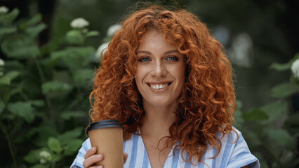 Naklejka premium cheerful redhead woman holding paper cup outdoors.
