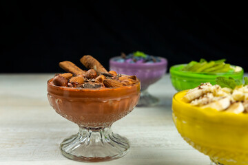 Smoothie or pudding with chocolate, hazelnuts and almonds served in a bowl for breakfast with several other smoothies in background