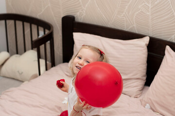 European little blonde girl in bed with red balloons. Valentine's day concept.