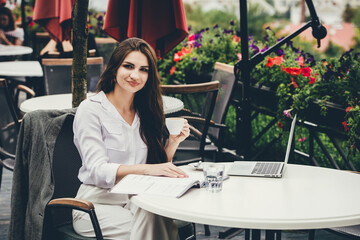 Young freelancer woman using laptop computer sitting at cafe table. Smiling woman working online or studying and learning while using notebook.