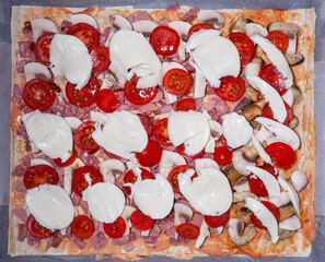 Homemade pizza on baking sheet with ham, mushrooms, mozzarella cheese, cherry tomatoes. Italian...