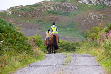 Couple horseback riding in Wales UK wearing safety gear to be seen by other road users and following Highway Code rule.