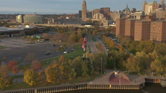American flag waving against Buffalo NY urban skyline, aerial flyby with zoom