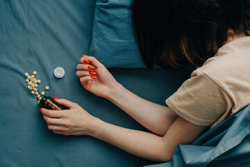 Medicines are scattered on the bed in front of the unrecognizable woman. Top view.