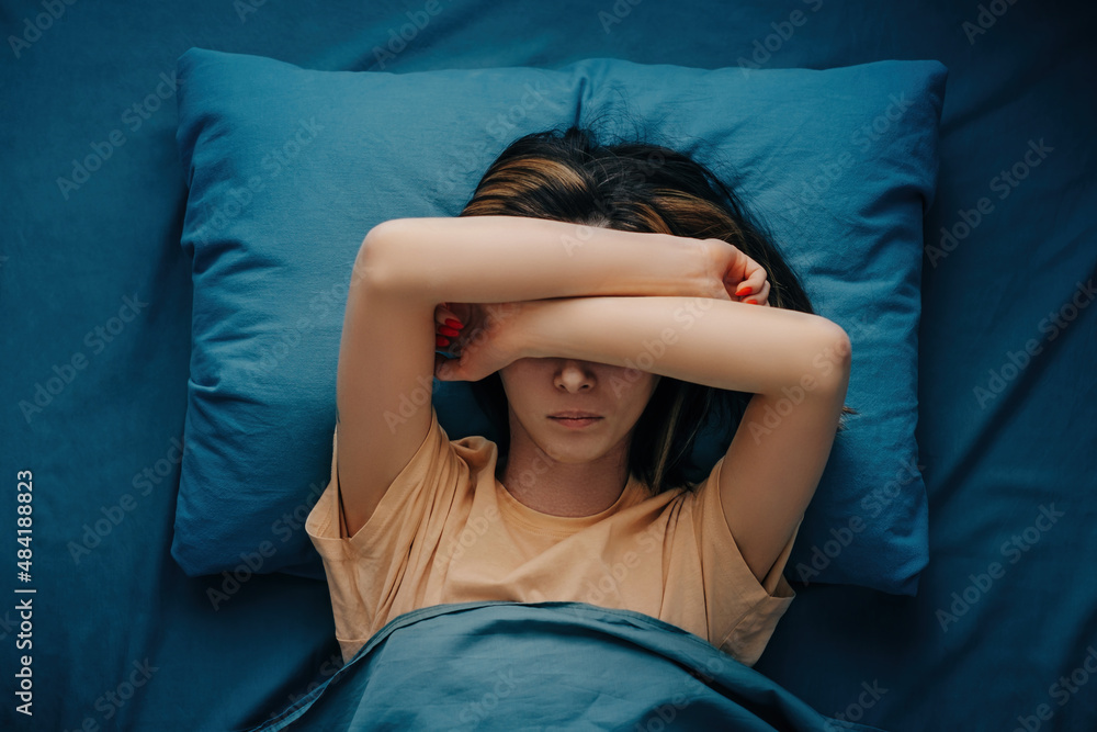 Wall mural A woman with a headache or migraine lies in bed. Top view.