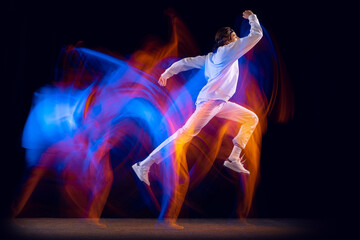 Flexible man in sports white suit dancing hip-hop isolated on dark background in mixed neon light. Youth culture, hip-hop, movement, style and fashion, action.