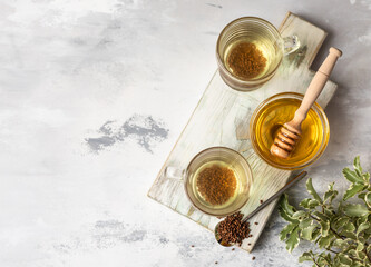 Cup with buckwheat tea, granules and honey, light grey background. Superfood Taiwan Ku Qiao buckwheat tea and grits of tartary buckwheat. Detox and healthy food.