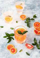 Gin and tonic alcohol drink with blood Sicilian oranges and ice on blue background. Cold refreshing cocktail.
