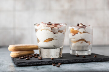 Traditional Italian dessert tiramisu in glass. Coffee flavored portion dessert made of savoiardi and mascarpone decorated with cocoa powder.