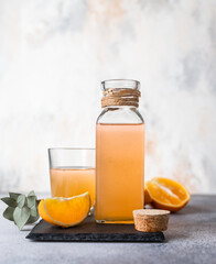 Orange lemonade in glass and bottle with fresh orange. Refreshing summer drink. Cocktail bar background concept.