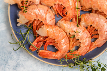 Raw red Argentine shrimps on ceramic plate, blue background. Ocean jumbo shrimps. Top view.