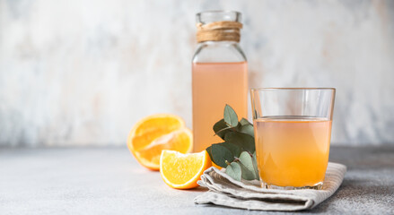 Cold and refreshing fresh orange juice in glass and bottle with fresh orange, grey background. Copy space.