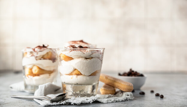 Traditional Italian dessert tiramisu in glass. Coffee flavored portion dessert made of savoiardi and mascarpone decorated with cocoa powder.