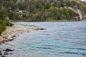 Lake in Argentinian Patagonia with turquoise water and trees in the background between mountains. Cloudy day with clouds between the mountains.
