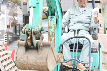 工事現場で重機に乗りガッツポーズをする作業員の男性（カメラ目線）