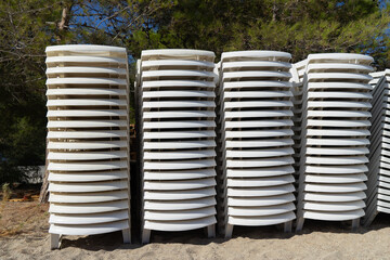 Beach loungers plastic white are stacked on top of each other on the ground. Preparation for the beach tourist season