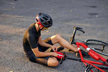 Naklejka premium young caucasian man with knee injury while cycling on forest road during the summer time, health care problem concept. unhappy man wearing helmet and suffering from knee ache,using medicine chest