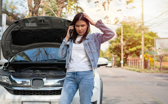 Angry Asian Woman And Using Mobile Phone Calling For Assistance After A Car Breakdown On Street. Concept Of Vehicle Engine Problem Or Accident And Emergency Help From Professional Mechanic