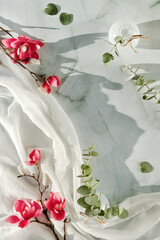 Pink magnolia flowers and green eucalyptus twigs on soft off white textile scarf. Wintertime, springtime background.