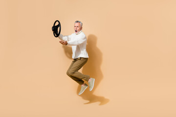 Fototapeta na wymiar Full length body size view of attractive outraged man jumping holding steering wheel shout isolated over beige pastel color background