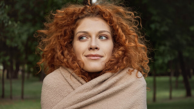 pleased redhead woman with blue eyes covered in blanket outside.