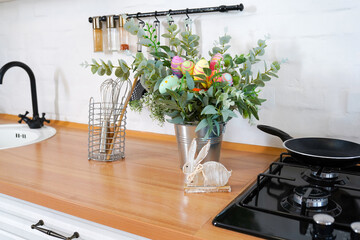 Easter bunny and bouquet with flowers and eggs on wooden table in Scandinavian-style kitchen. Beautiful Easter greeting card