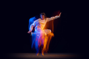 Dynamic portrait of male hip-hop dancer dancing isolated on dark background in mixed neon light. Youth culture, hip-hop, movement, style and fashion, action.