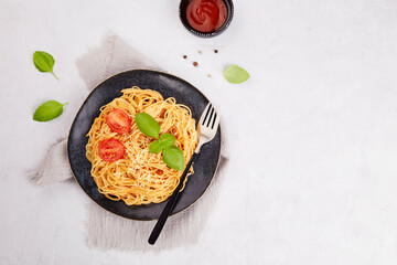 Classic Italian pasta spaghetti with tomatoes, tomato sauce, basil on a dark plate on a light gray background. Top view, copy space.