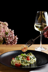 risotto with pesto, basil and cherry tomatoes closeup in black plate on wooden table. risotto on wooden table restaurant with glass of wine