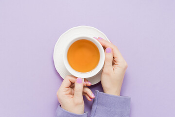 Female hands with purple nails holds cup of tea on purple background top view. Motivated by the...