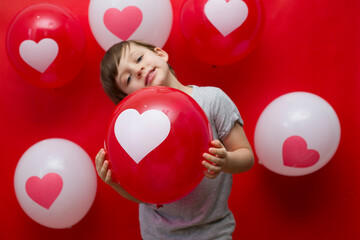 The boy with heart balloons congratulates with valentine's day, on a red background.