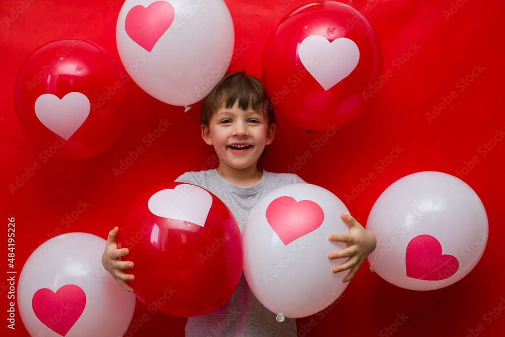 Wall mural The boy with heart balloons congratulates with valentine's day, on a red background.